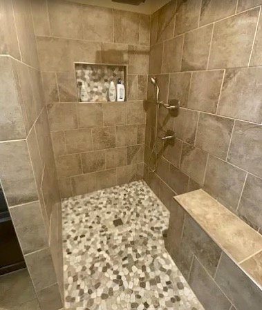 Stone-look walk-in shower with bench, niche, and pebble floor