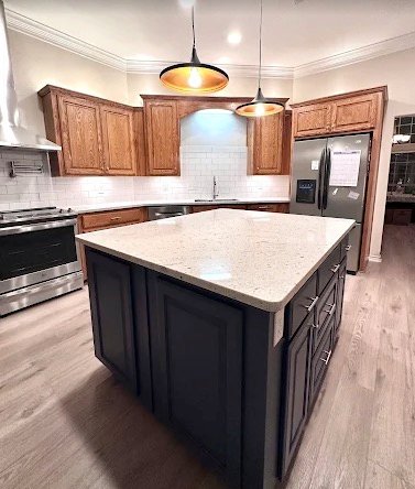 Kitchen remodel with black island, wood cabinets, pendant lights, and quartz counters